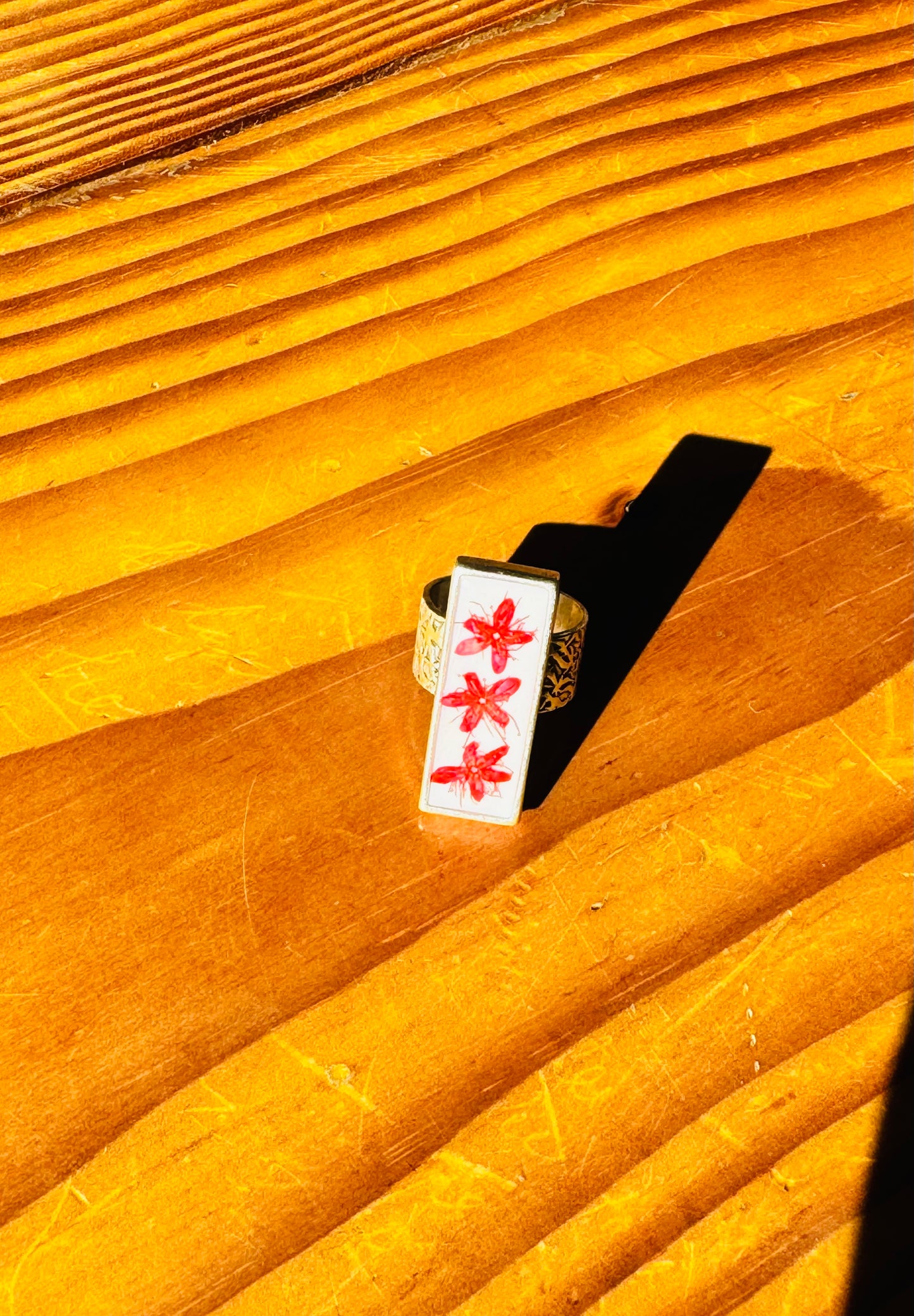 Rectangular long silver ring with red flower on a white background