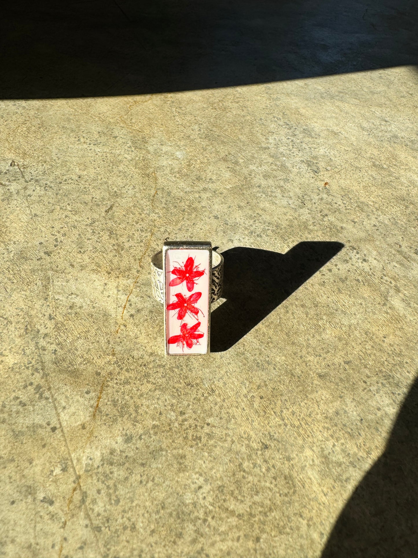 Rectangular long silver ring with red flower on a white background