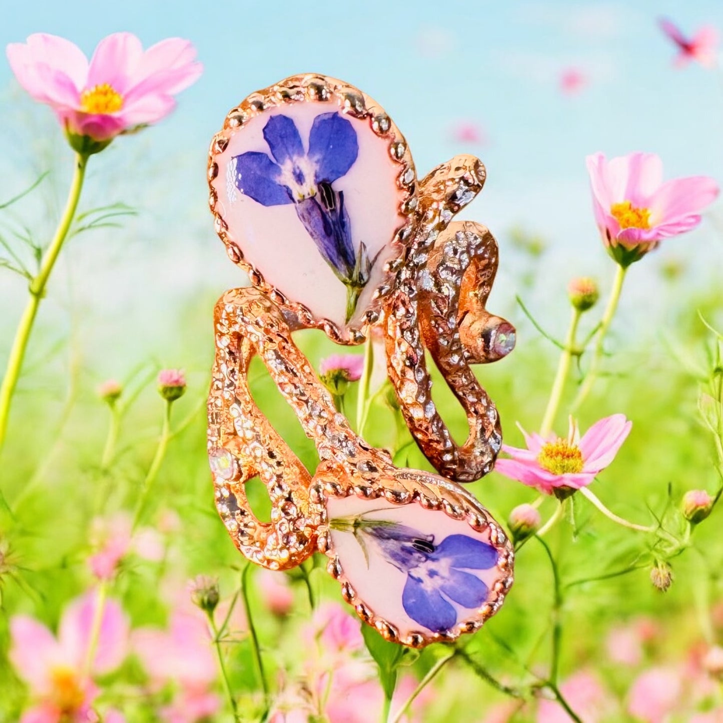 Oversized pink gold plated ring with blue flowers on a white background