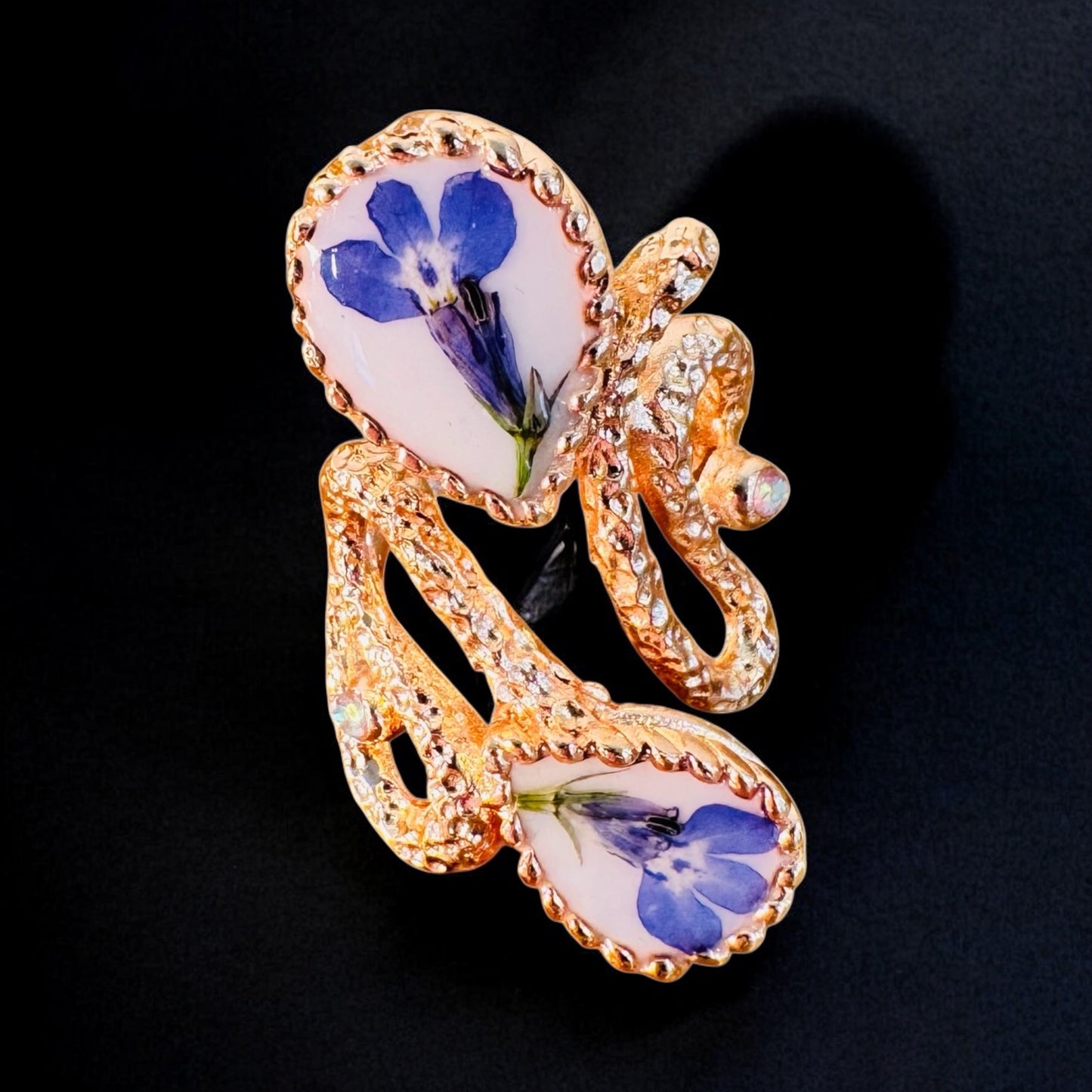 Oversized pink gold plated ring with blue flowers on a white background