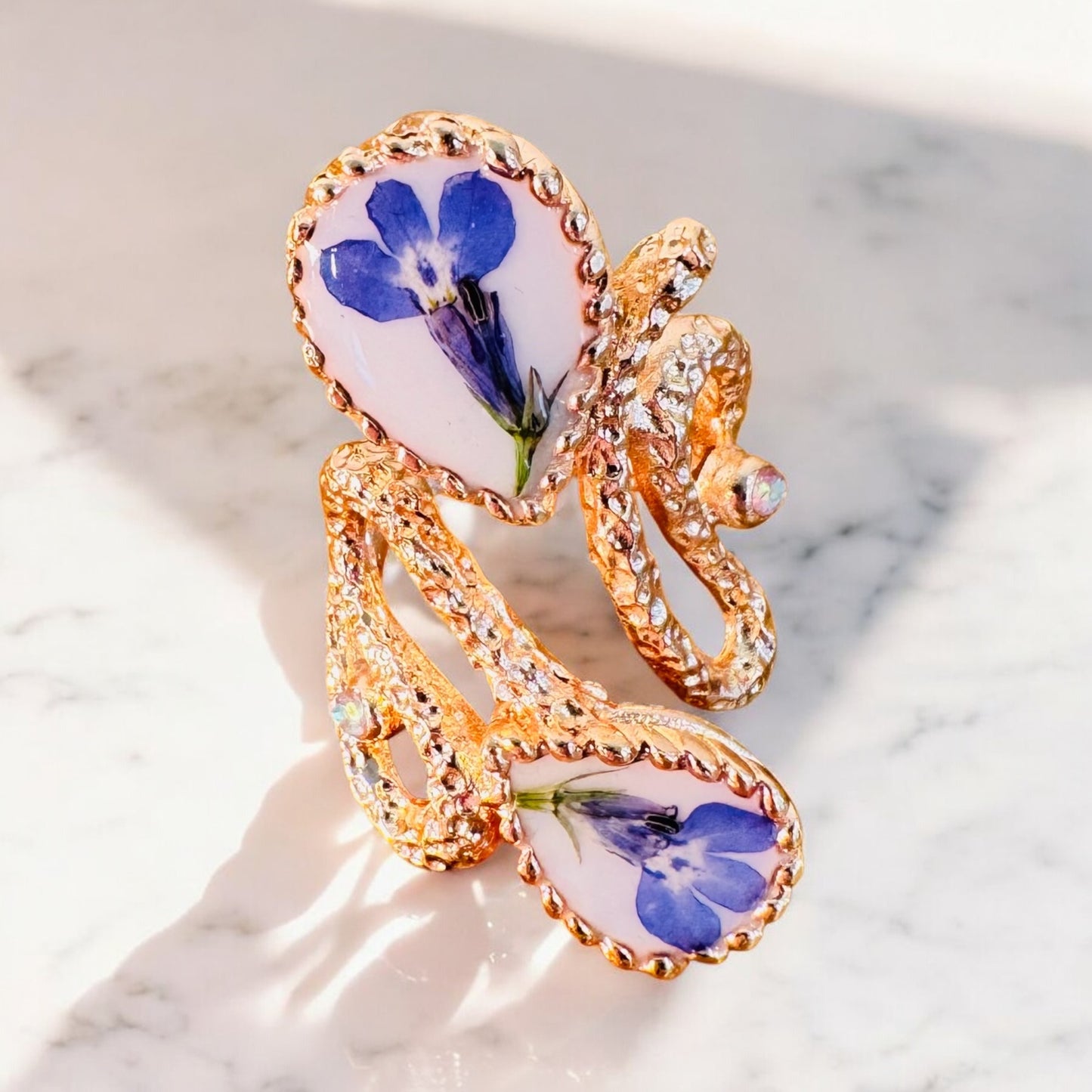 Oversized pink gold plated ring with blue flowers on a white background