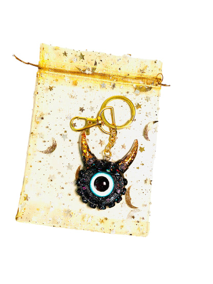 Black and gold one eyed monster keychain. Model Vicky.