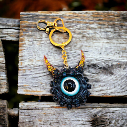 Black and gold one eyed monster keychain. Model Vicky.