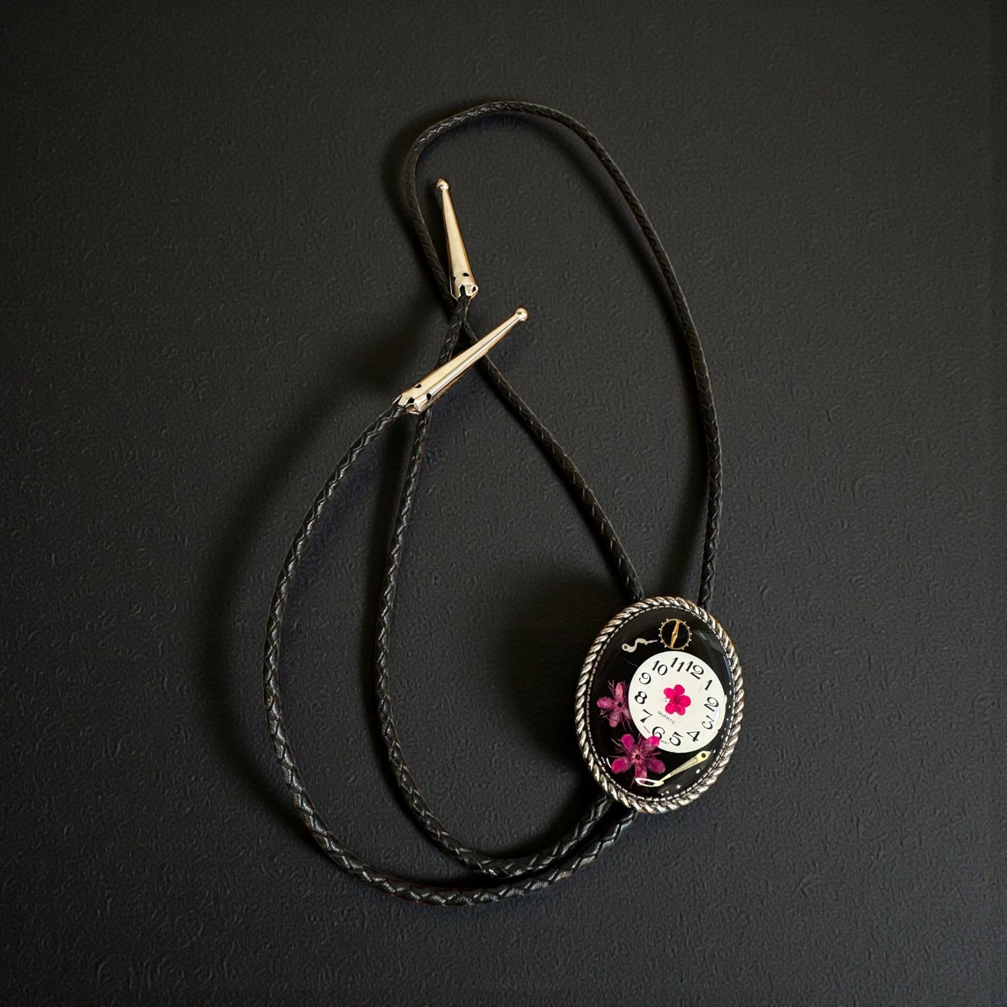 Bolo tie, pink flower and watch gears on black background
