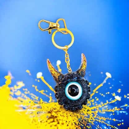 Black and gold one eyed monster keychain. Model Vicky.