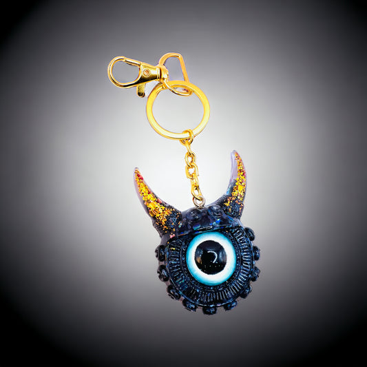 Black and gold one eyed monster keychain. Model Vicky.