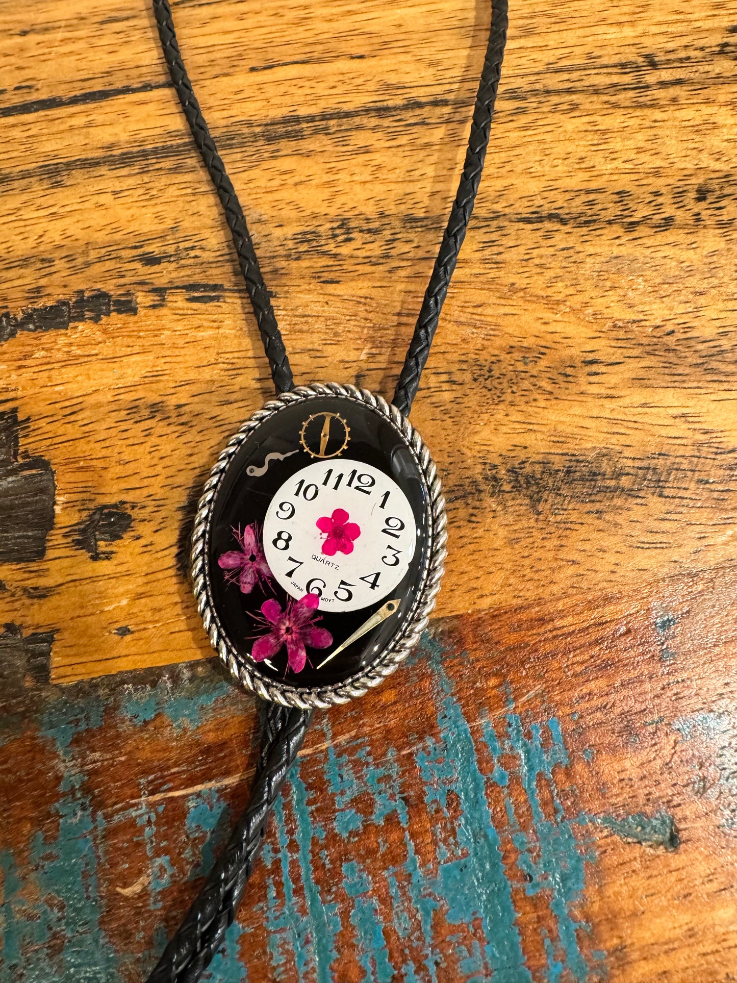 Bolo tie, pink flower and watch gears on black background
